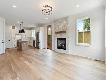 Open living, dining, and kitchen with stone fireplace and backyard access-CJMC Build at 2703 Bronte Ave, Nashville.