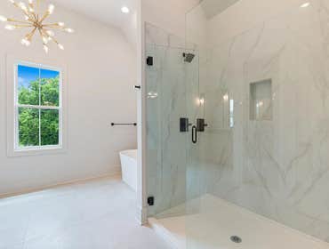 Spacious primary bath at 1135 Delmas Ave, East Nashville: glass walk in shower, freestanding soaking tub, and vaulted ceiling with modern lighting by C
