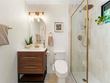 Cody & Katie | Primary Bathroom This primary bathroom remodel features a warm, modern design with soft neutral tile, brushed brass fixtures, and a waln