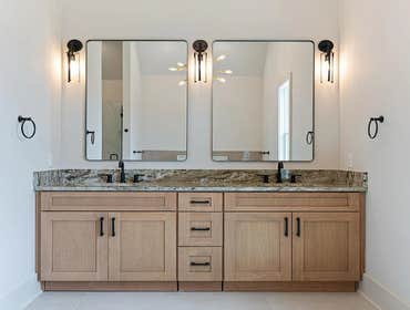 Primary bath dual vanity at 1135 Delmas Ave, East Nashville: natural wood cabinetry, stone tops, and matte black faucets by CJMC Build.