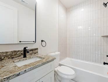 Guest bathroom at 1135 Delmas Ave, East Nashville by CJMC Build: stone vanity top, framed mirror, and vertical stack subway tile surround.