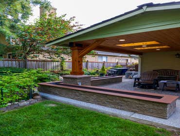 Holmer Project Wood patio cover over deck in backyard. Estimated size is about 14x14. Wooden beams/posts, skylights, asphalt roofing, cedar wood ceilin