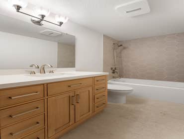 Kun | Bathroom This Redmond bathroom remodel combines warmth and modern elegance. The space features a natural wood vanity with sleek brushed nickel fi