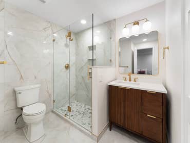 Tracy | Master Bathroom This master bathroom remodel features large-format marble-look tile, a frameless glass shower, and warm brushed gold fixtures. 