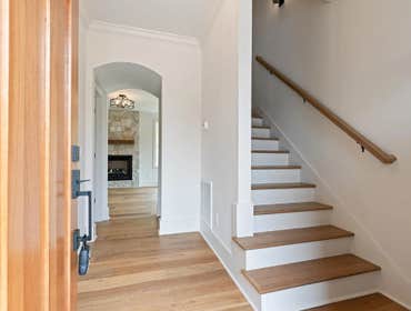 Entry view with wood stairs, wide plank floors, and stone fireplace sightline at 2703 Bronte Ave by CJMC Build.