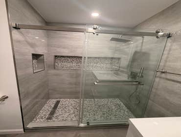 Modern bathroom remodel with a clean, upgraded finish This bathroom was transformed with a walk-in shower, large gray tile, pebble-style shower floor, 