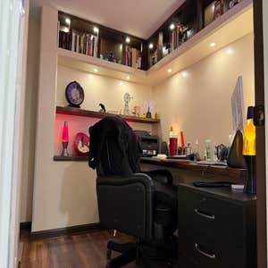 Custom built-in home office with a walnut desk surface, floating shelves with accent LED lighting, and upper display shelving with recessed puck...