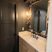Bold, color-drenched basement bathroom featuring moody dark walls paired with statement floral wallpaper, a gold-framed mirror, globe sconce lighting, 