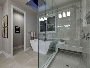 Glass walk-in shower with gray subway tiled surround and white freestanding tub in new luxury home