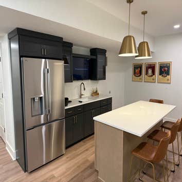 Custom wet bar with dark shaker cabinetry, quartz countertops, and a seating island anchored by brass pendant lighting. A built-in TV niche and full-si