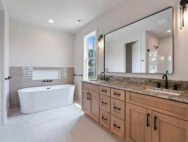 Primary bath with dual vanity, stone counters, soaking tub, and tile niche at 2703 Bronte Ave by CJMC Build.