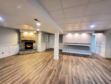 Lusby Basement Remodel A cozy and inviting basement designed for both style and function. The standout stone fireplace creates a warm focal point, whil